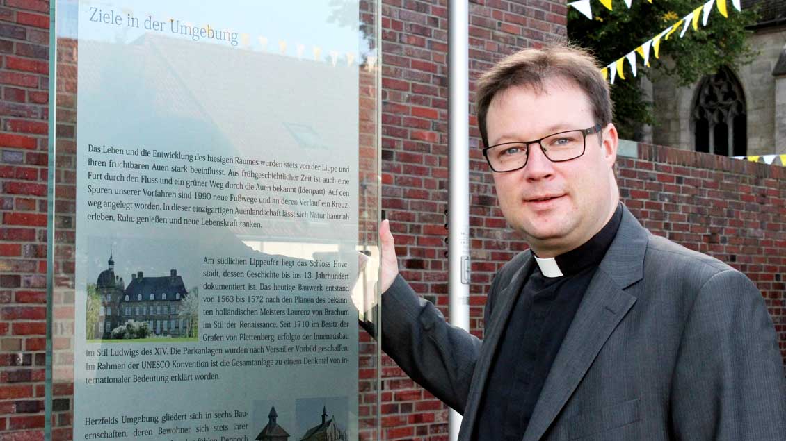 Pfarrer Joachim Kosmann vor einer Glasstele in der Dorfmitte von Herzfeld..